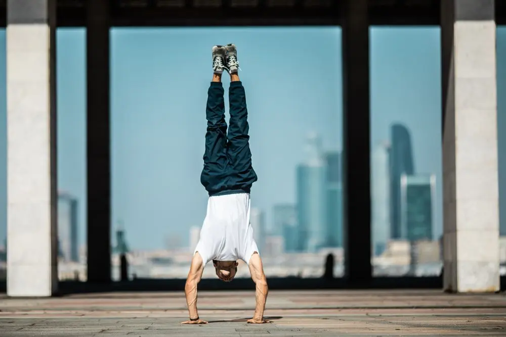 Man holding a freestanding handstand with a city skyline behind him