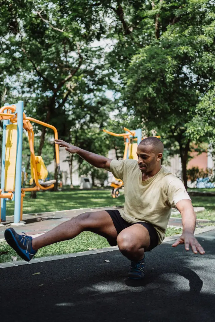 Man at the bottom of a pistol squat in a park, one leg extended